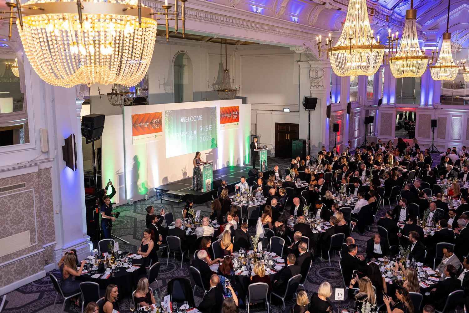 Large formal awards ceremony in grand ballroom with guests seated at round tables.