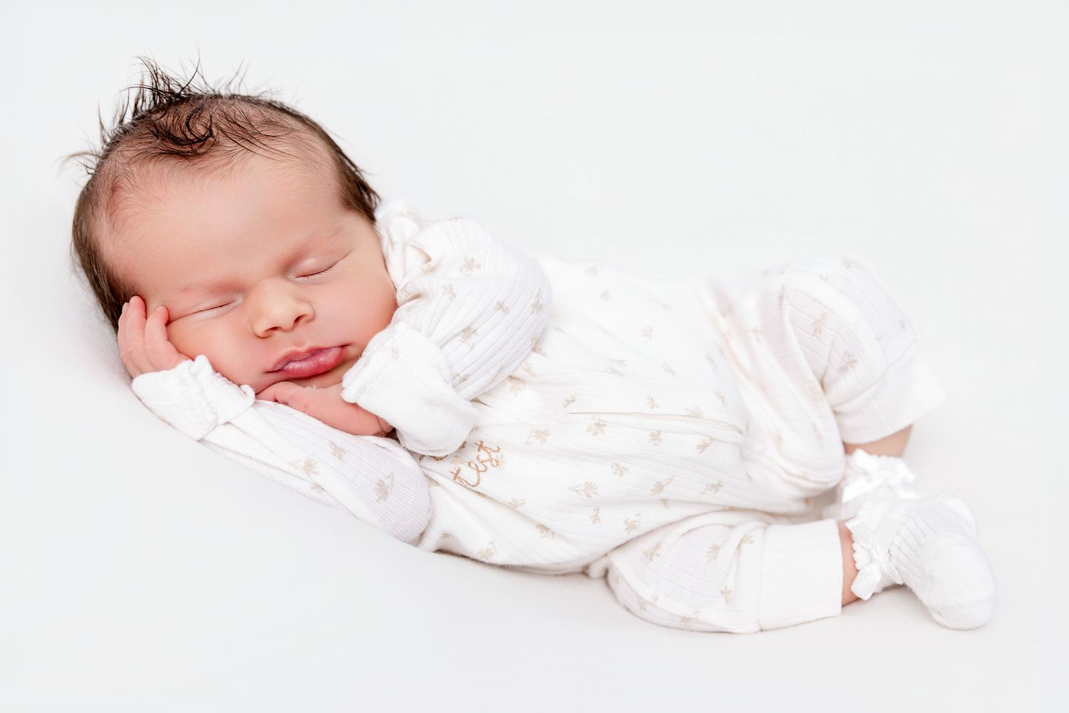 Peaceful sleeping newborn baby in white star print outfit, curled on white background.