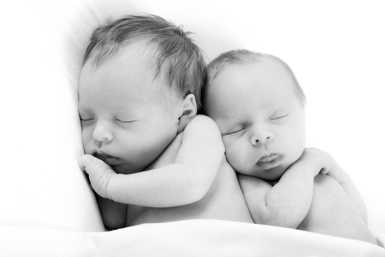 Two sleeping newborn twins cuddled together in a tender black and white portrait photo.