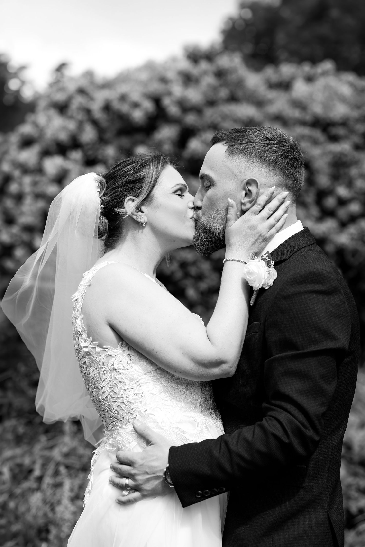 Black and white photo of a bride and groom sharing a romantic kiss on their wedding day outdoors.