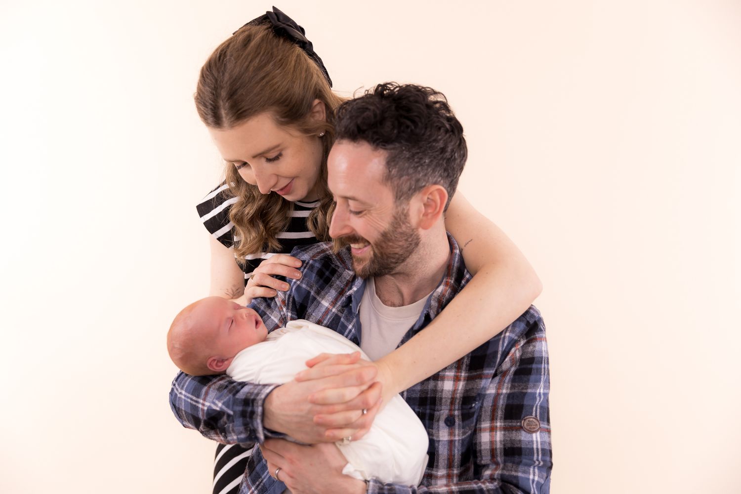 Happy new parents smiling and holding their newborn baby during a studio photo session.