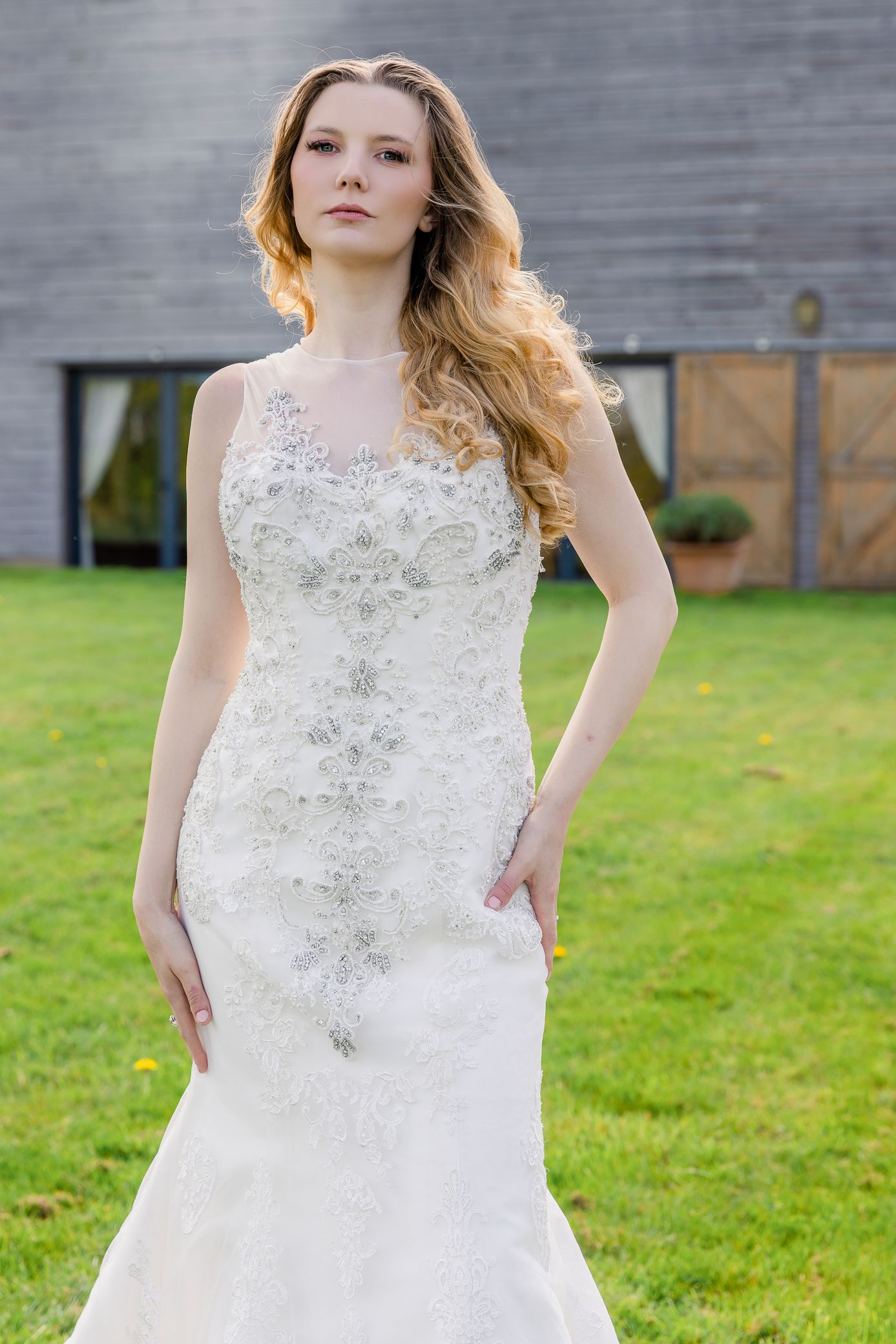 Bride in heavily embellished lace mermaid wedding dress posing outdoors with barn building background.