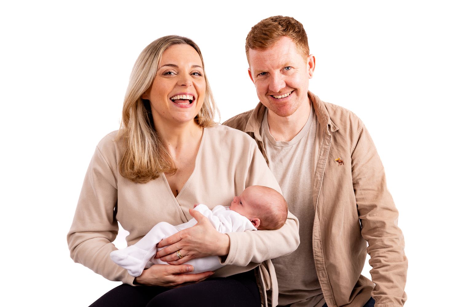 Happy parents laughing and smiling while holding their newborn baby against a white studio background.