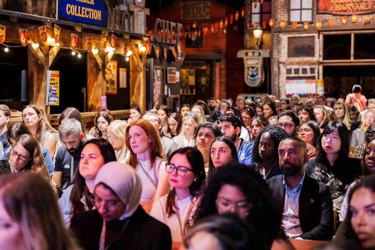 A large crowd of diverse attendees engaged at an indoor conference event with warm ambient lighting.