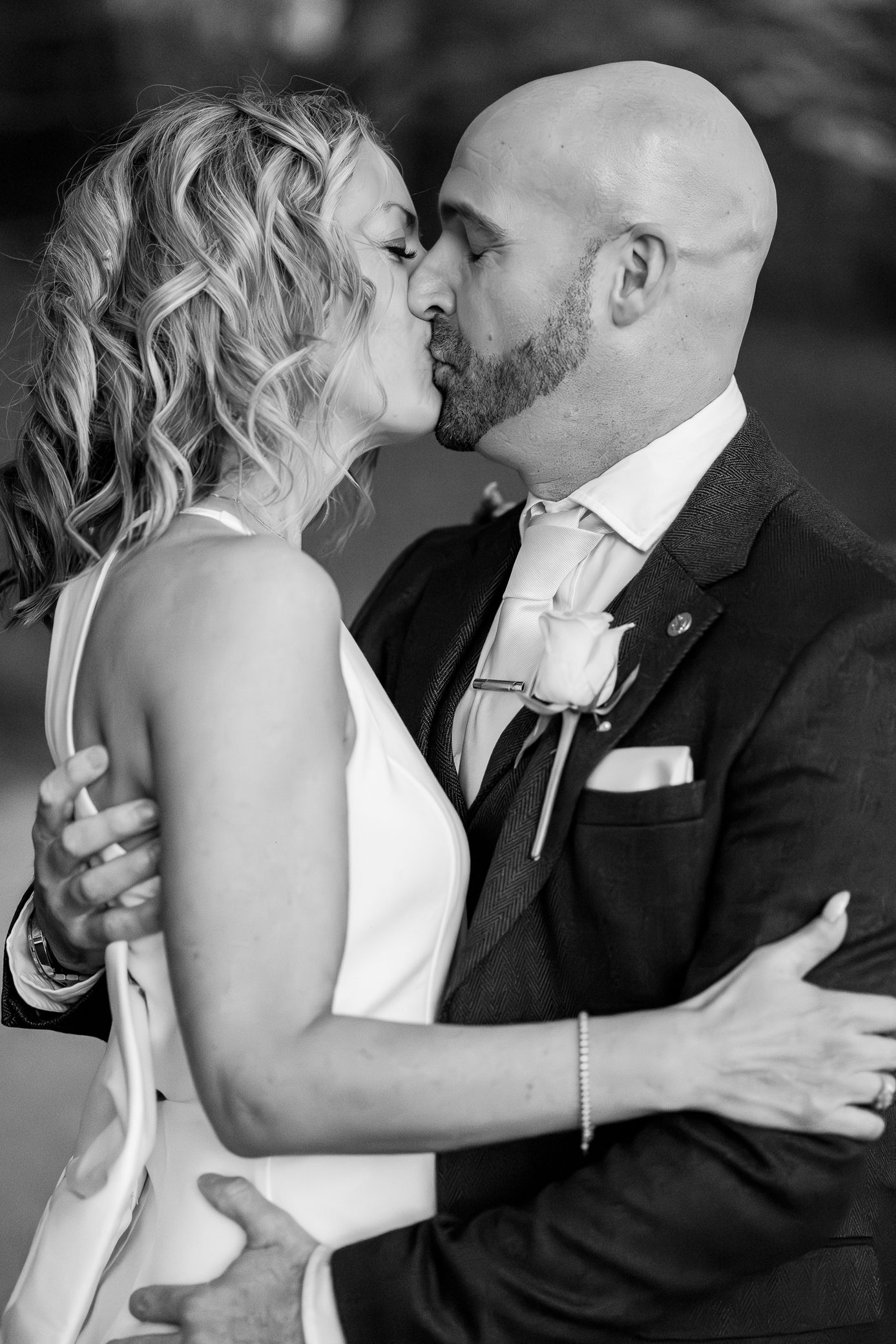 Bride and bald groom share passionate kiss in close-up black and white wedding portrait.