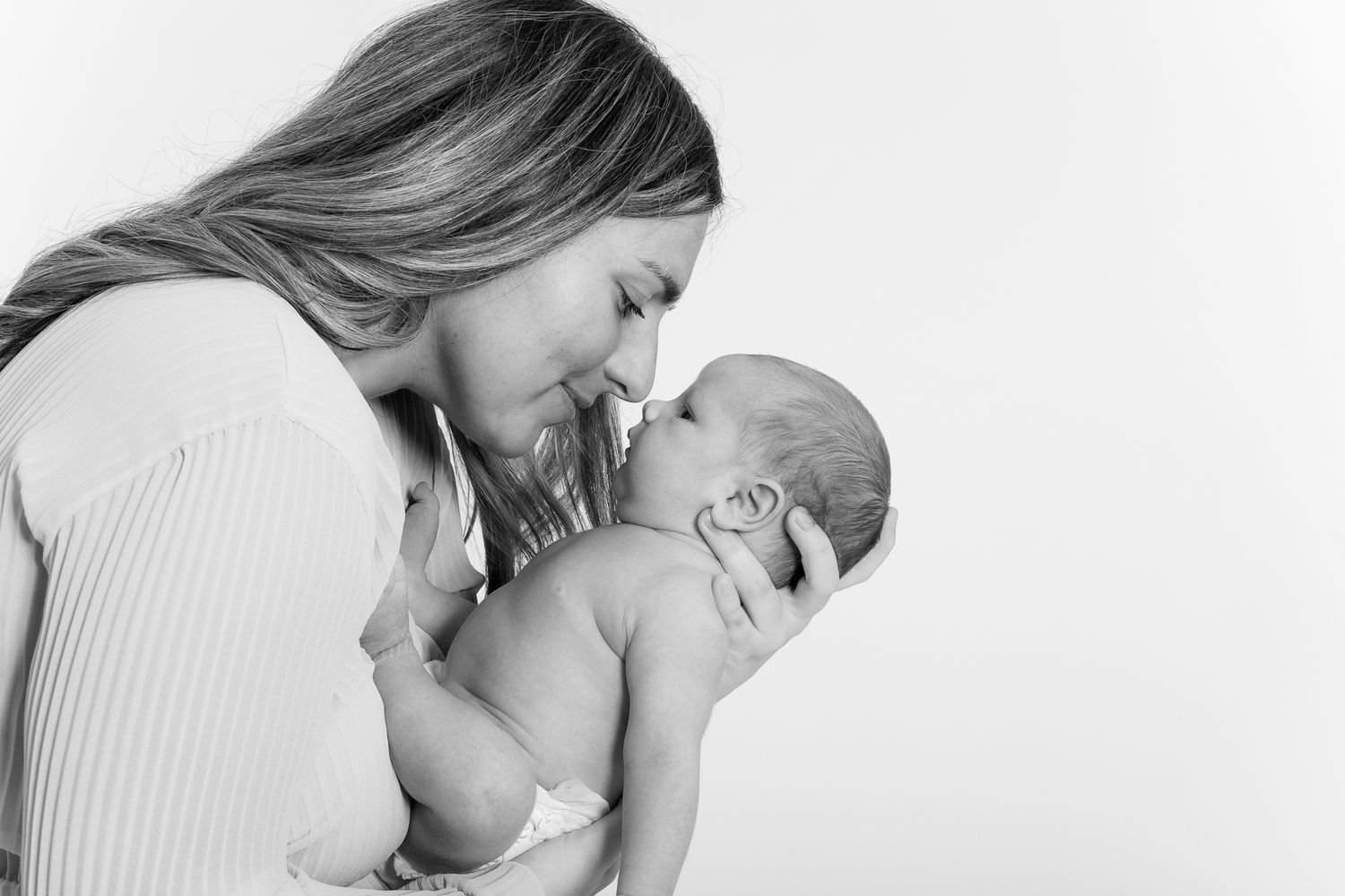 Black and white photo of a mother tenderly touching noses with her newborn baby.