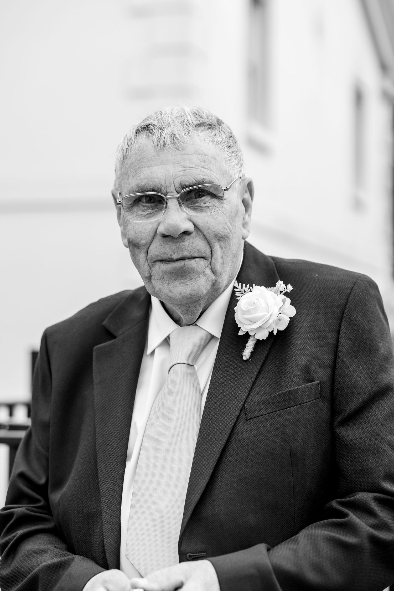 Elderly man in suit with boutonniere and tie poses for formal black and white portrait photo.