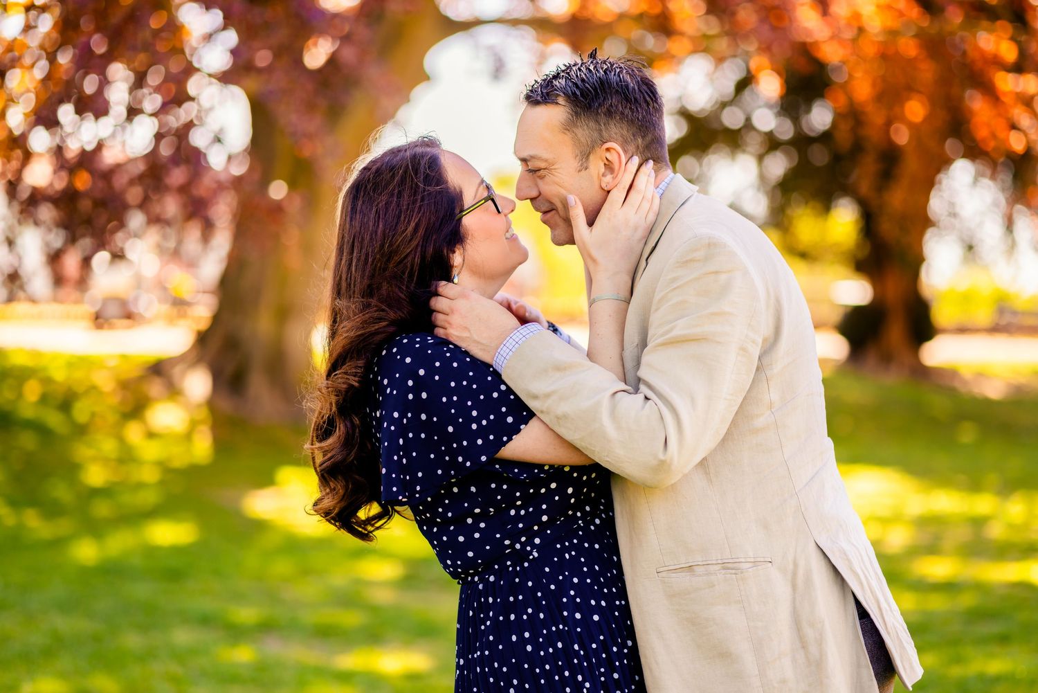 Couple embracing and laughing together outdoors in a park during autumn with colorful foliage in background.