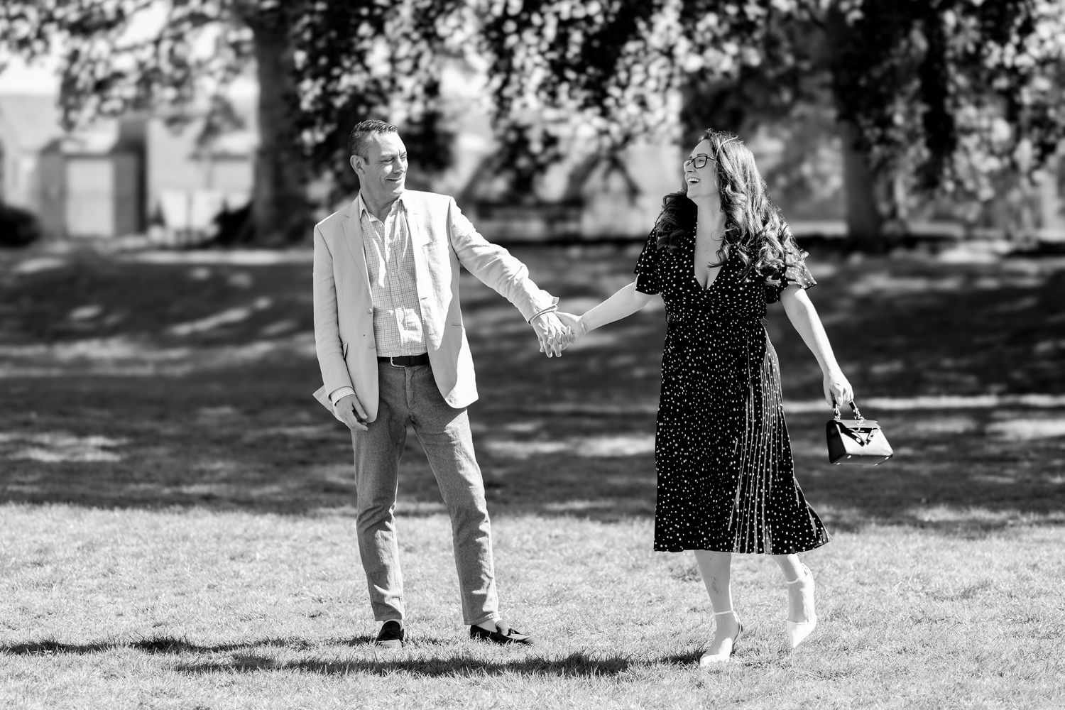 Black and white photo of a couple holding hands and spinning together in a sunny park.