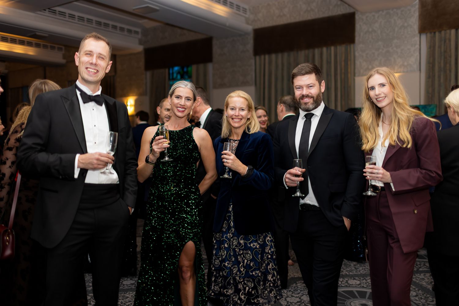 Group of five professionals in formal attire holding champagne glasses at a gala event.