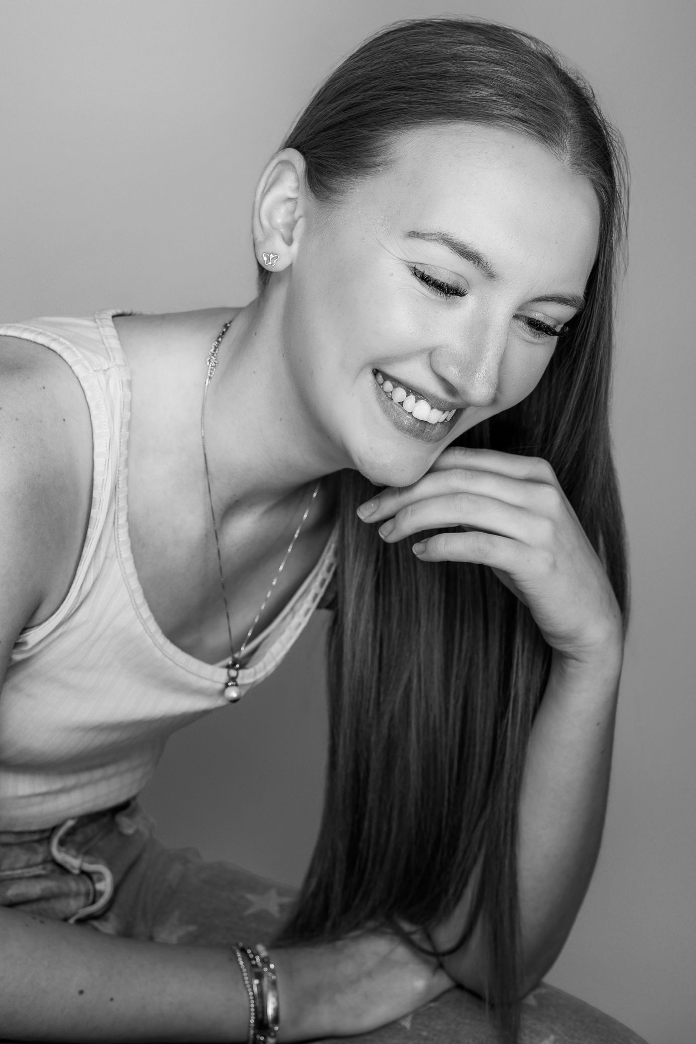 A young woman with long straight hair laughs candidly in a black and white studio portrait.