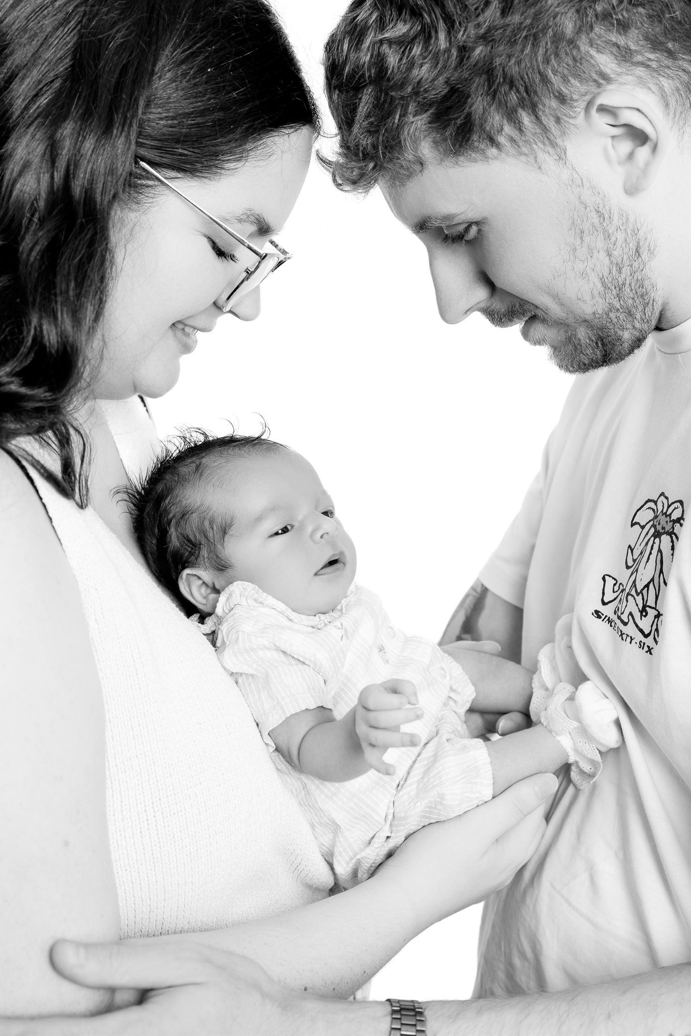 New parents lovingly gazing at their alert newborn baby, black and white family portrait.
