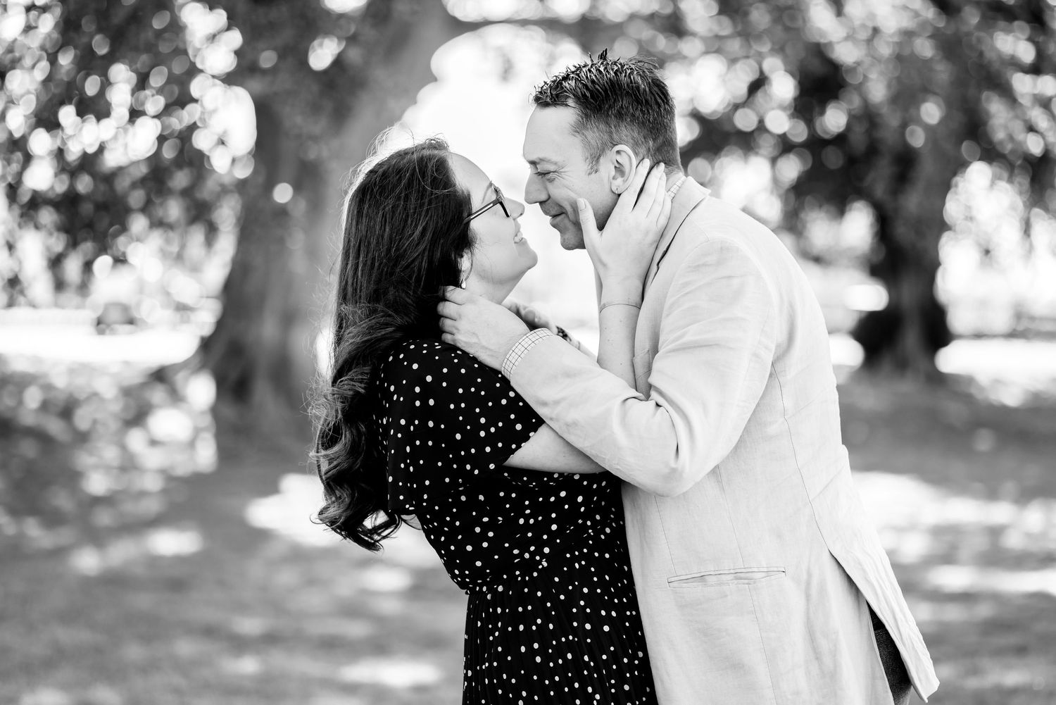 Black and white photo of a couple embracing and laughing together outdoors among trees.
