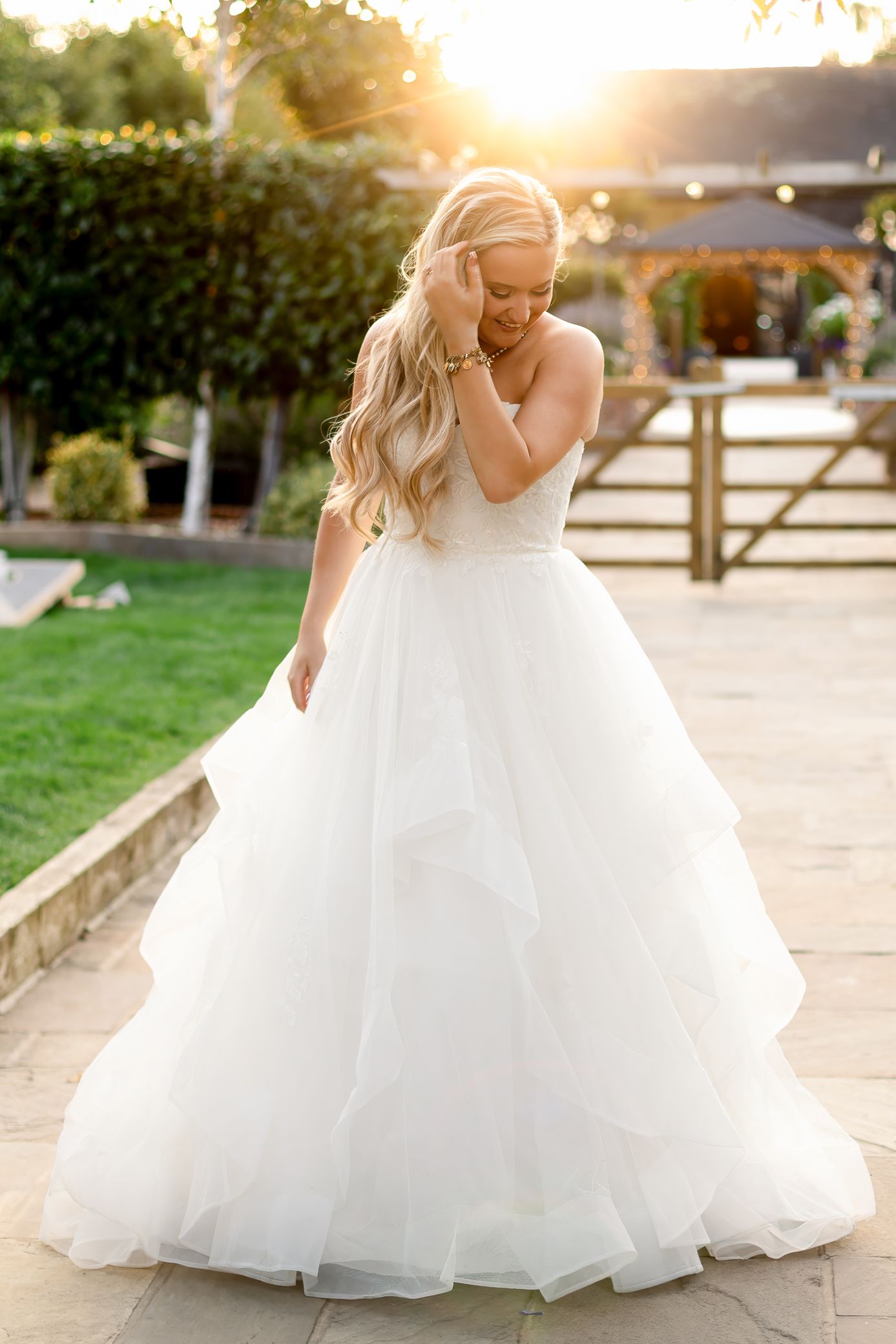 Bride twirls in a layered tulle ball gown at golden hour in a garden venue with string lights.