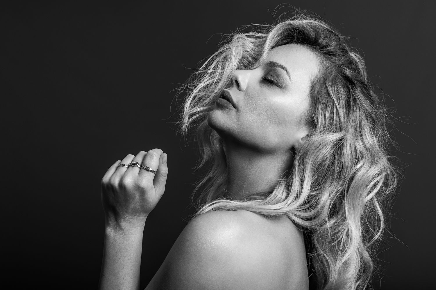 Elegant black and white photo of a blonde woman with wavy hair and stacked rings posing dramatically.