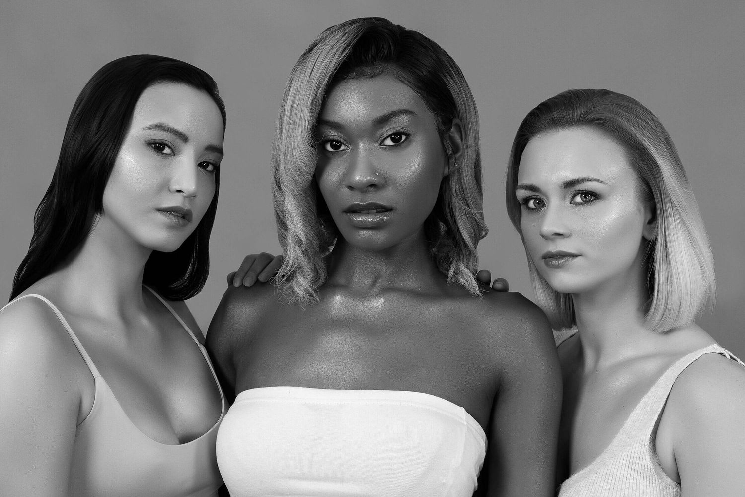 Black and white studio portrait of three diverse women in white tops posing together confidently.