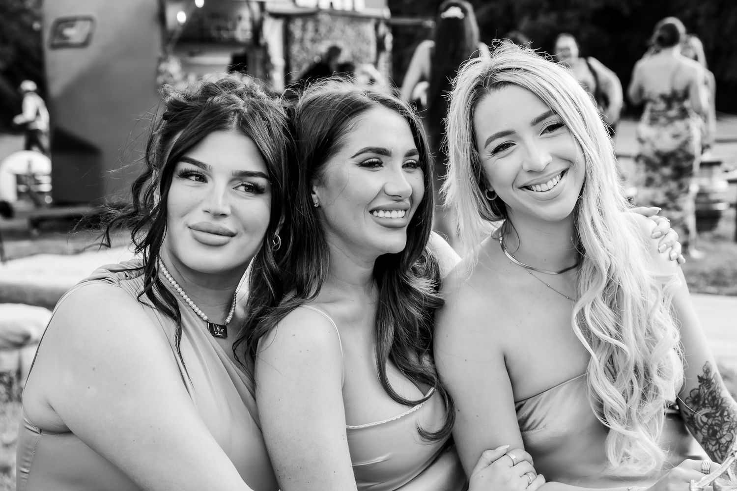 Three smiling women pose together at an outdoor wedding celebration in black and white photo.