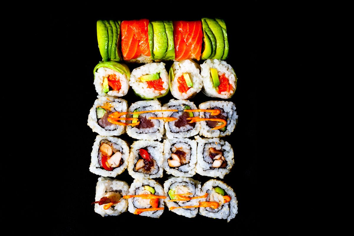 Assorted sushi rolls with avocado, salmon, and shrimp arranged on a black background.