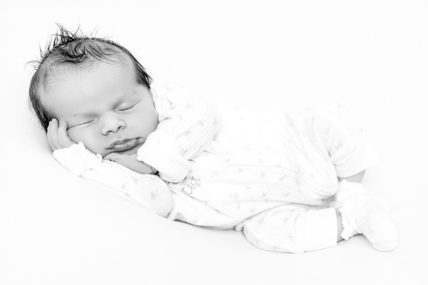 Sleeping newborn in white star print onesie, curled on side, black and white portrait.