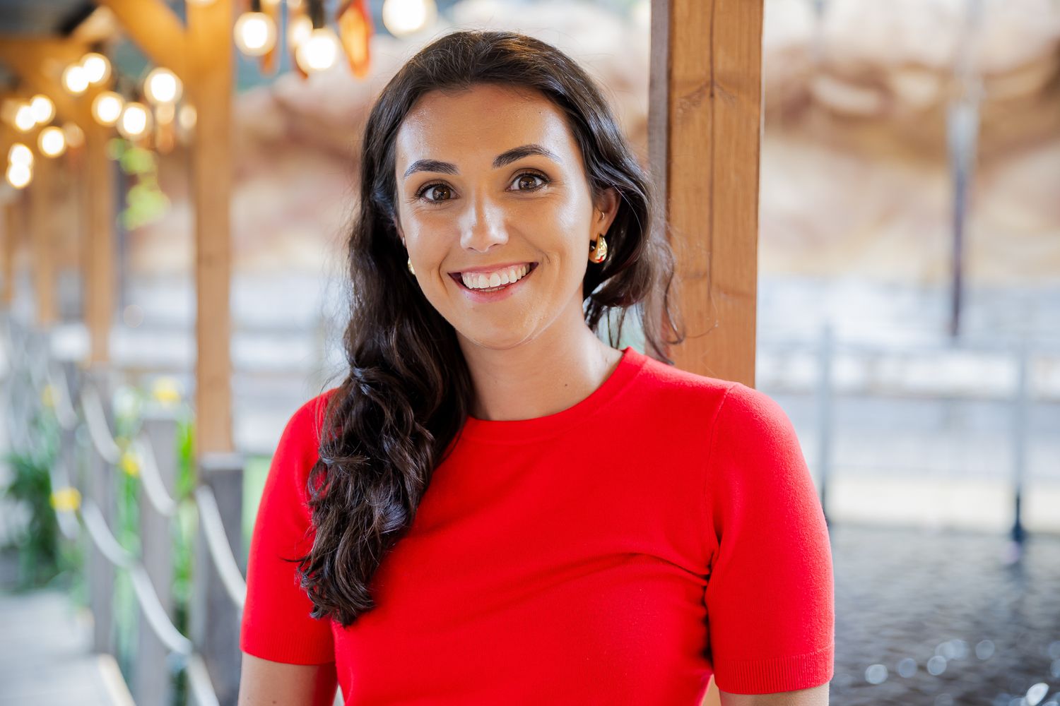 Smiling young woman with dark hair wearing a red dress posing in a warmly lit indoor venue.