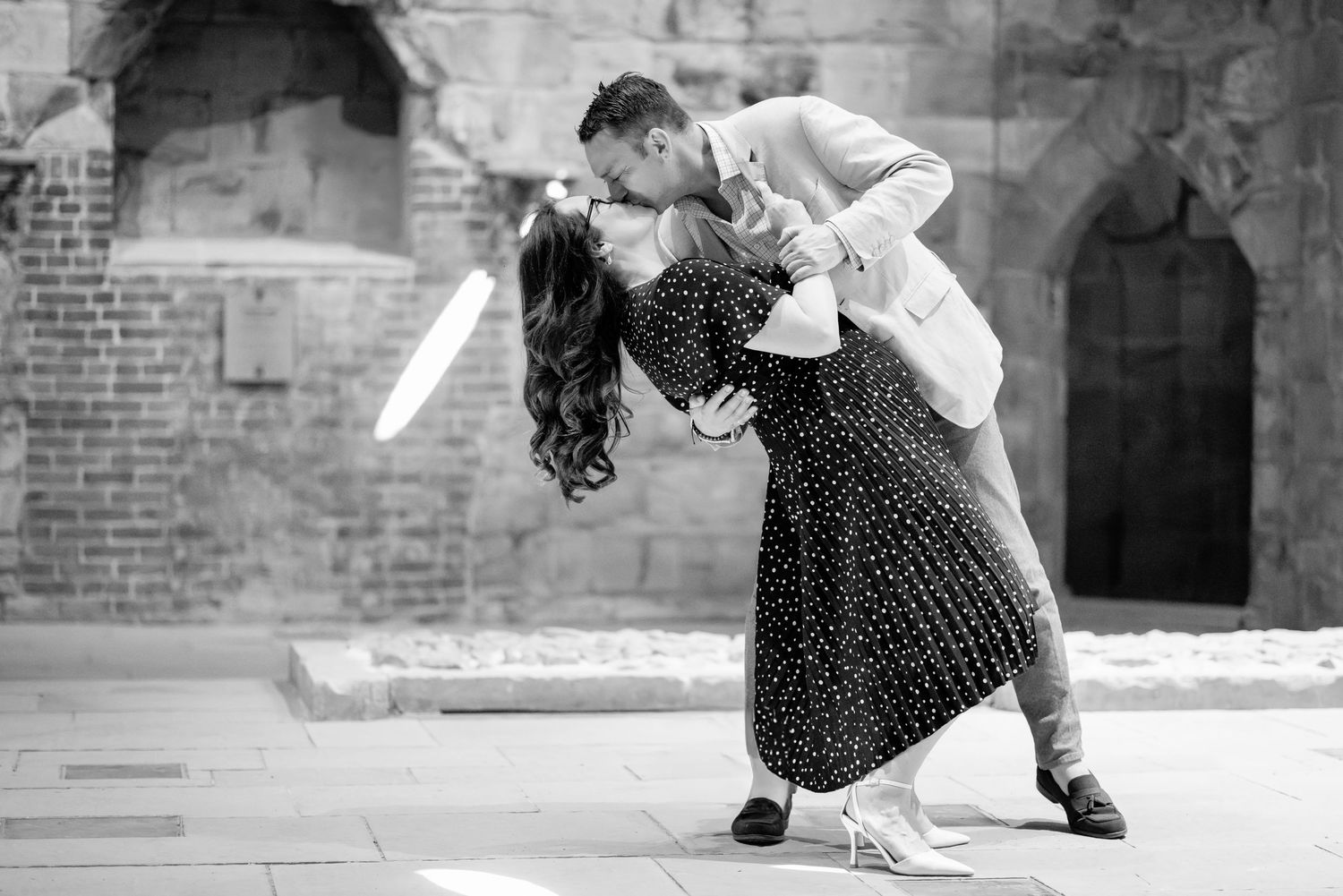 Couple sharing a romantic dip kiss in black and white photo outdoors near brick archway.