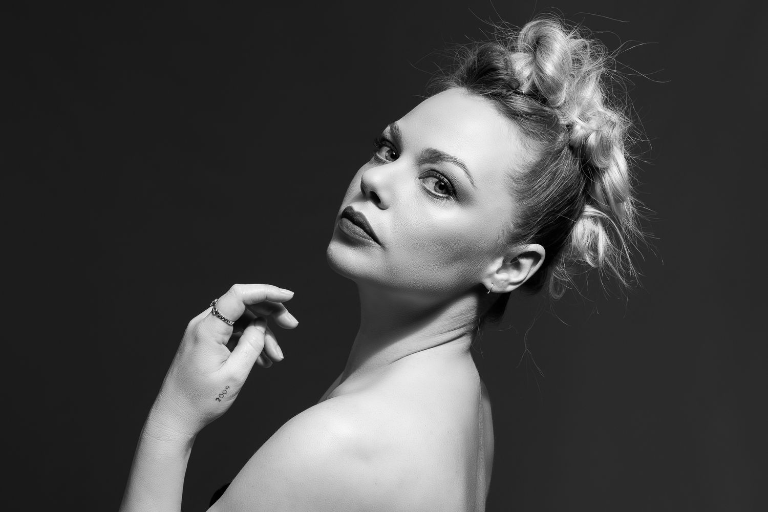 Black and white studio portrait of a blonde woman with updo hairstyle touching her chin gracefully.