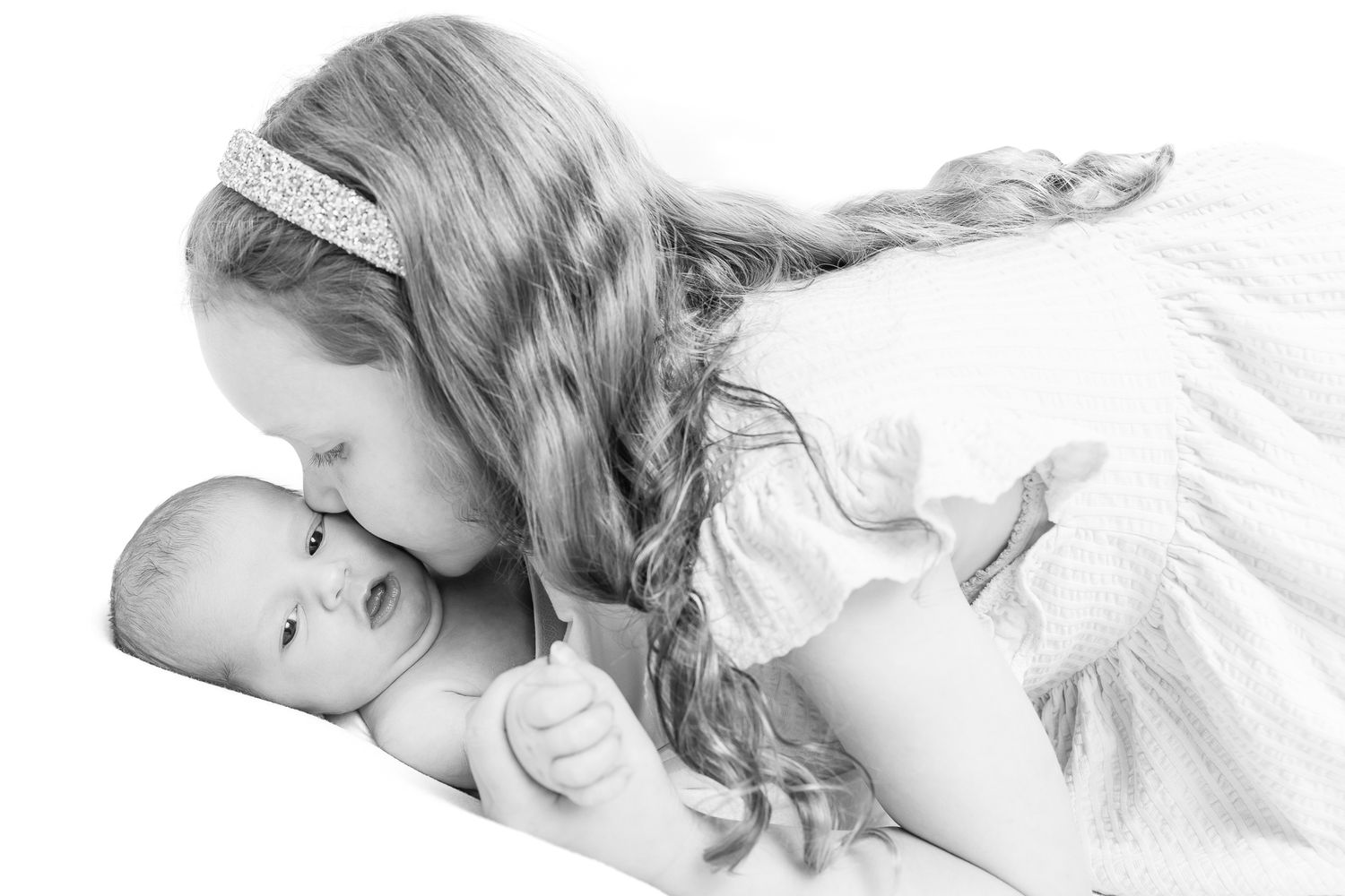 Young girl with long hair kissing a sleeping newborn baby in black and white.