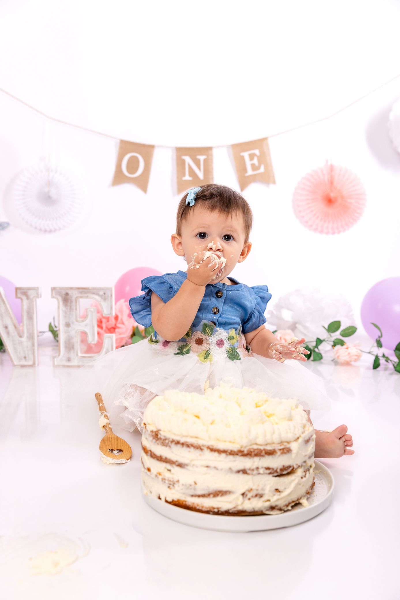 One year old baby girl eating smash cake at first birthday party with ONE banner decor.