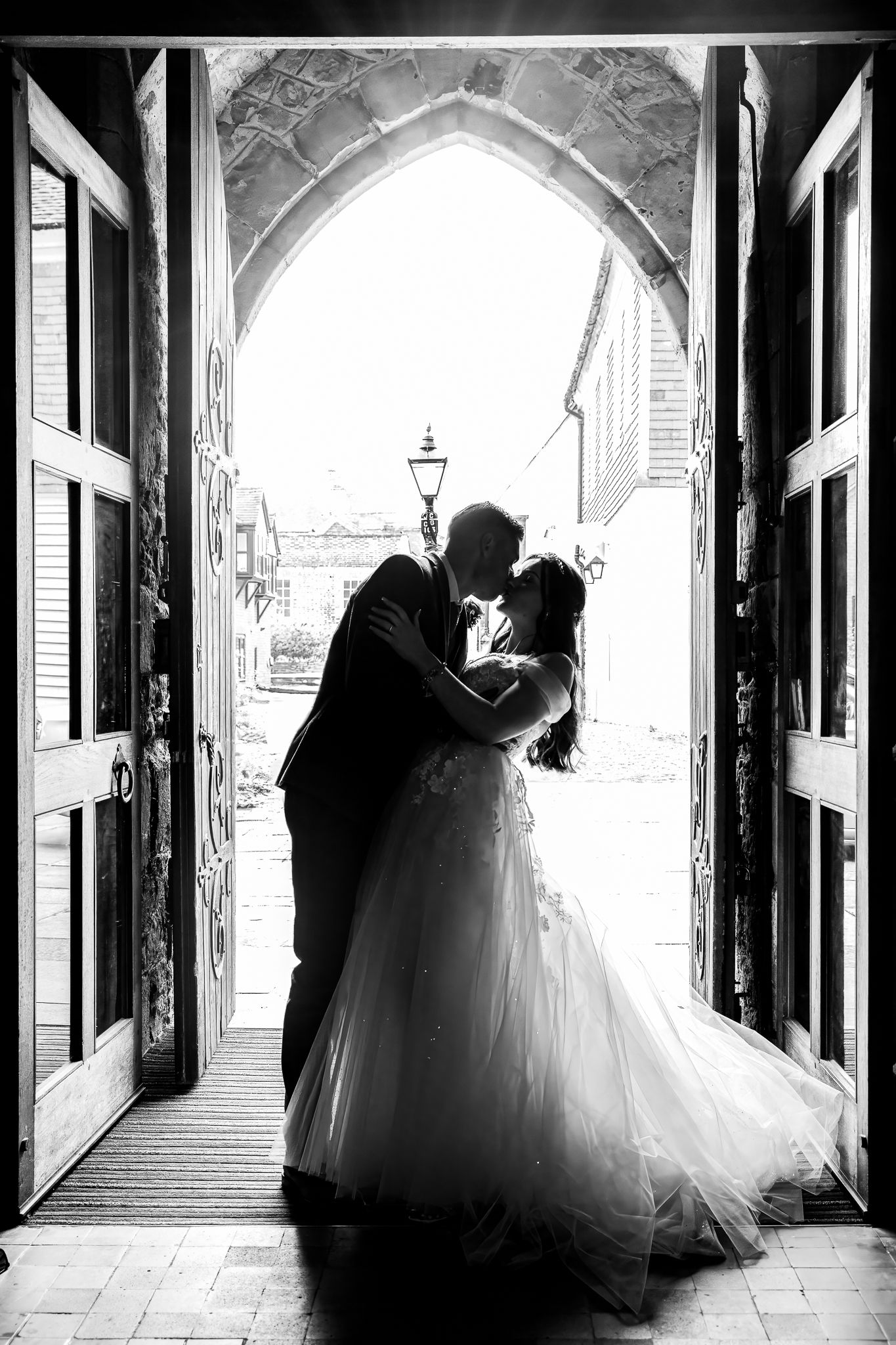 Silhouette of bride and groom kissing in arched church doorway, stunning black and white wedding photo.