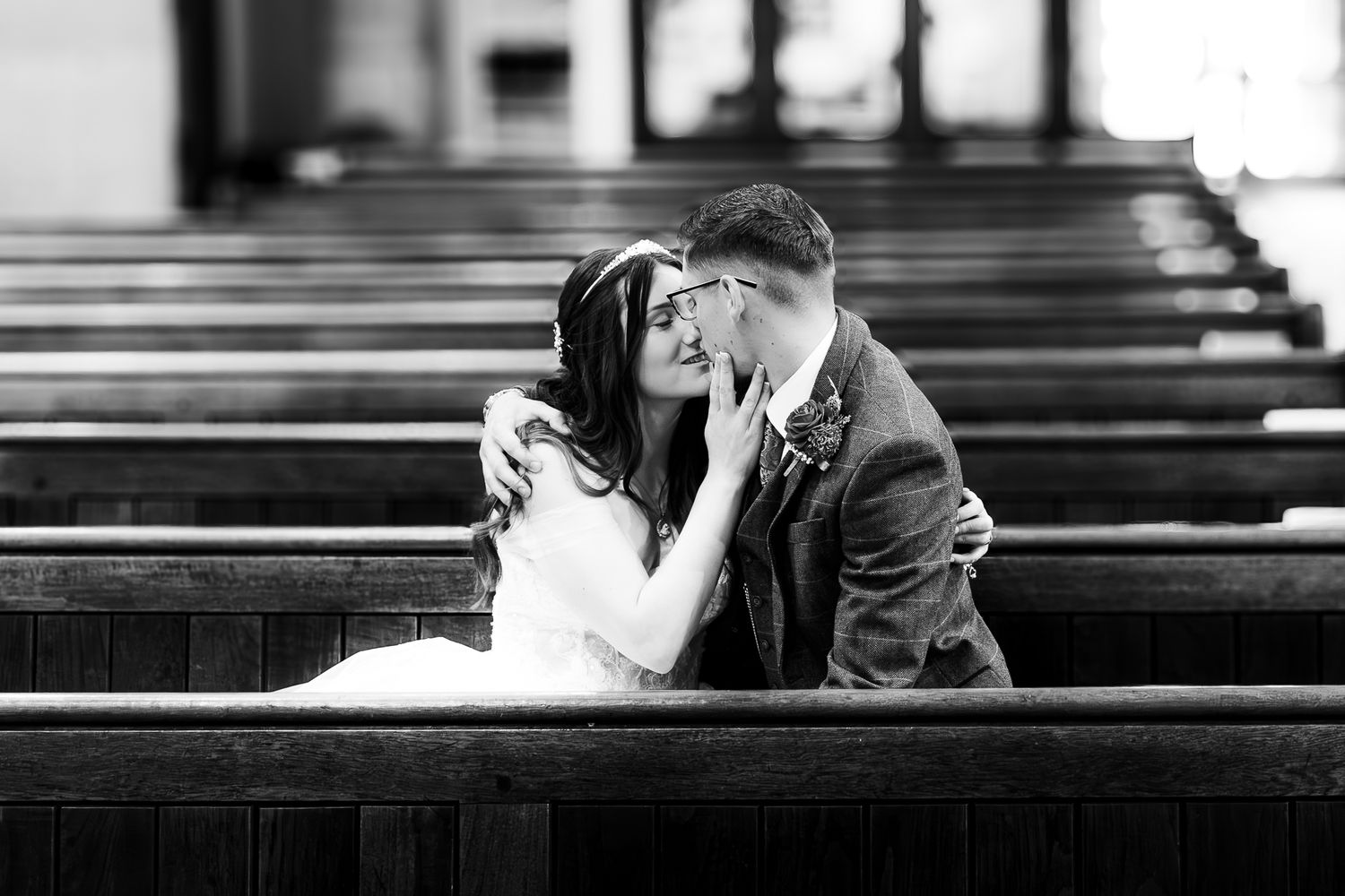 Bride and groom sharing intimate moment on church pew, romantic black and white wedding photography.