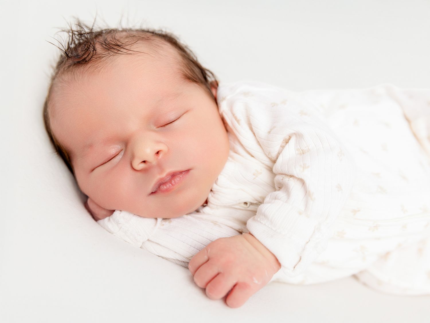 Peaceful newborn baby sleeping soundly wrapped in a soft white swaddle blanket.