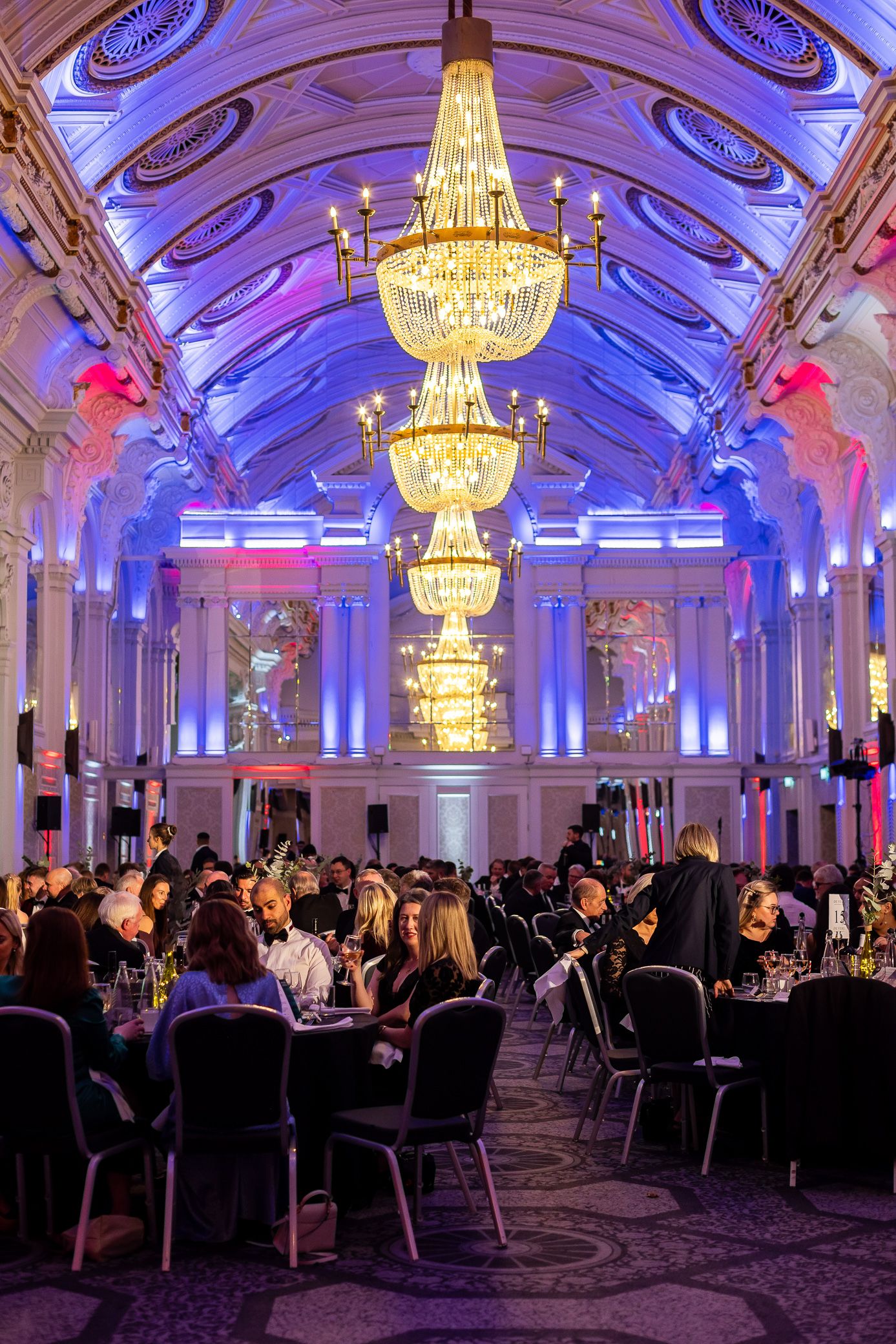 Elegant grand ballroom filled with guests dining under ornate crystal chandeliers.