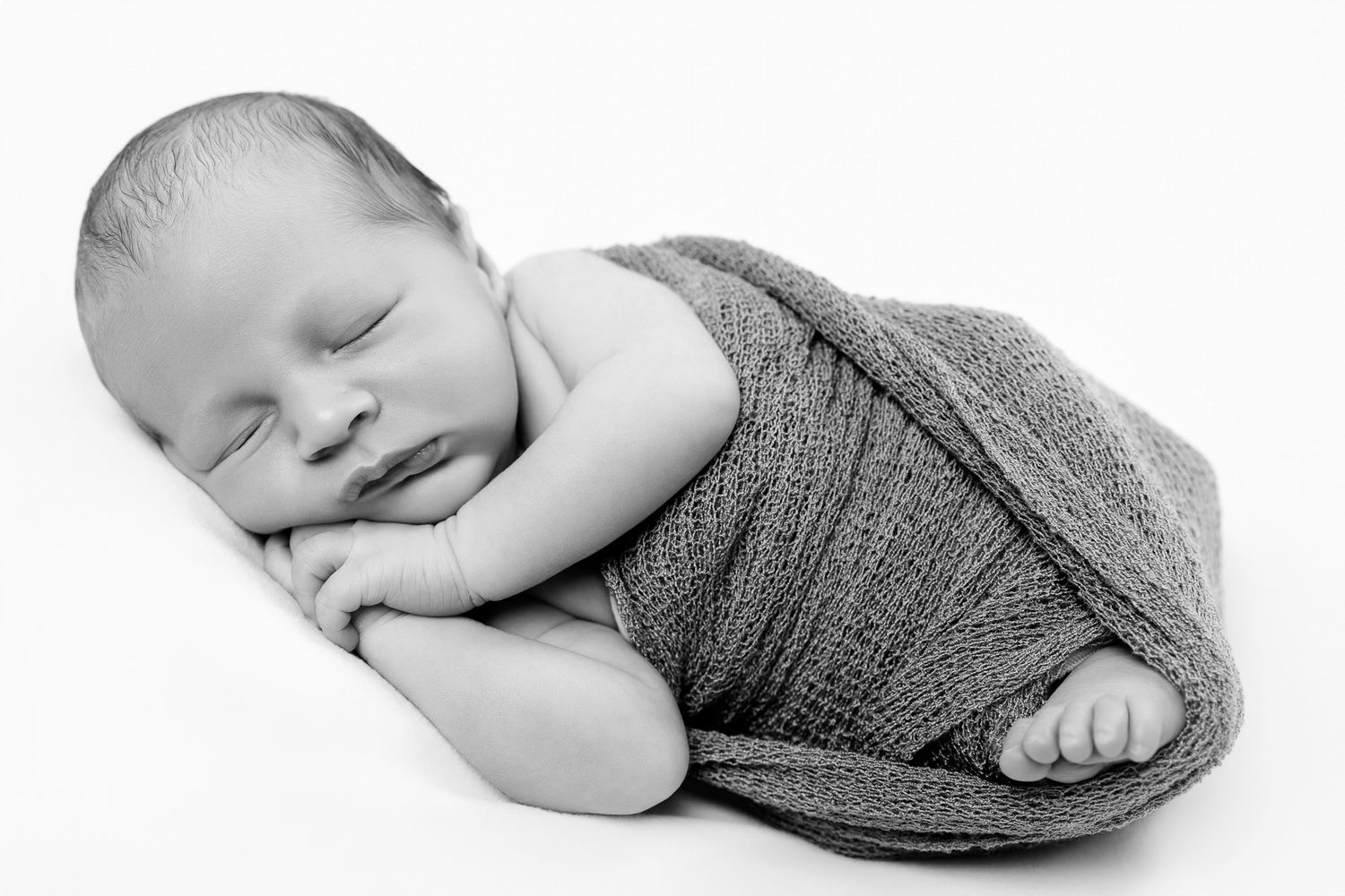Sleeping newborn baby wrapped in a gray knit blanket in black and white.