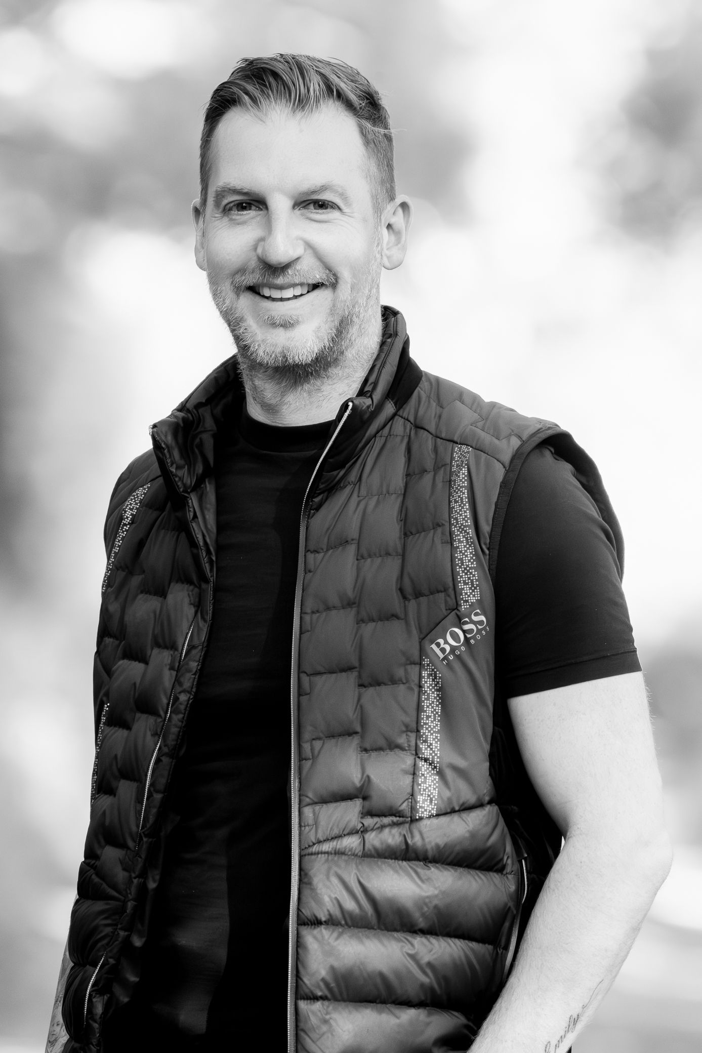 Smiling man in a Hugo Boss quilted vest posing outdoors in a black and white portrait photo.