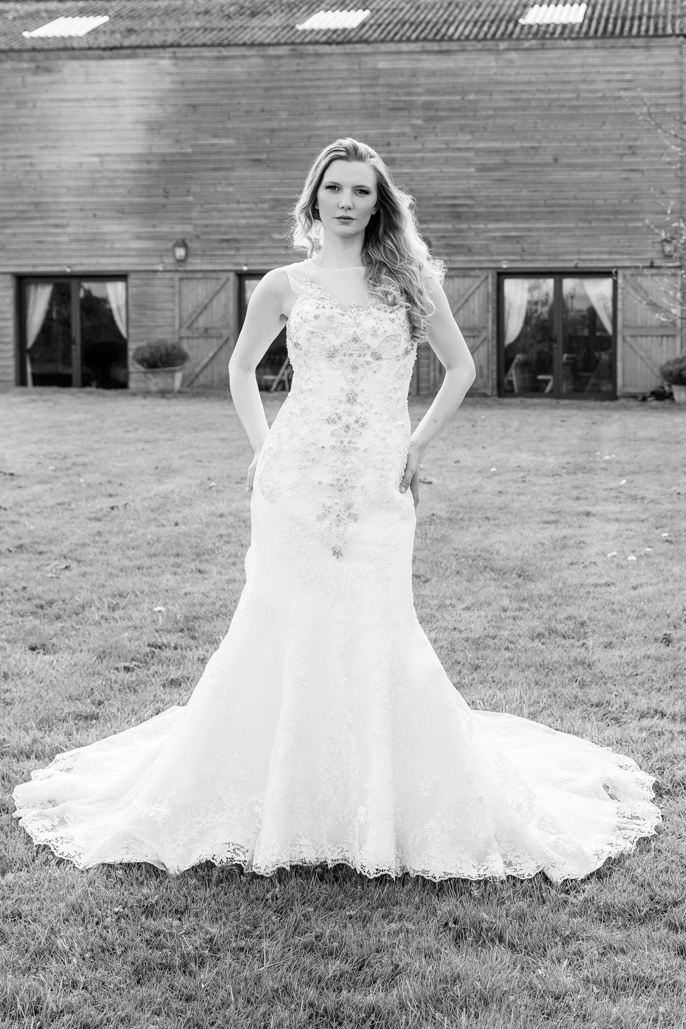 Elegant bride in fitted lace mermaid wedding gown posing outside rustic barn venue.