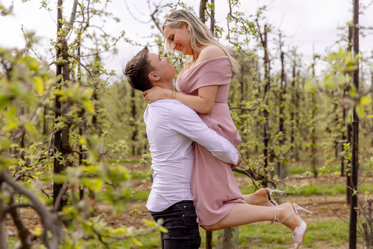 Couple sharing a romantic kiss in a blooming orchard during a spring engagement shoot.