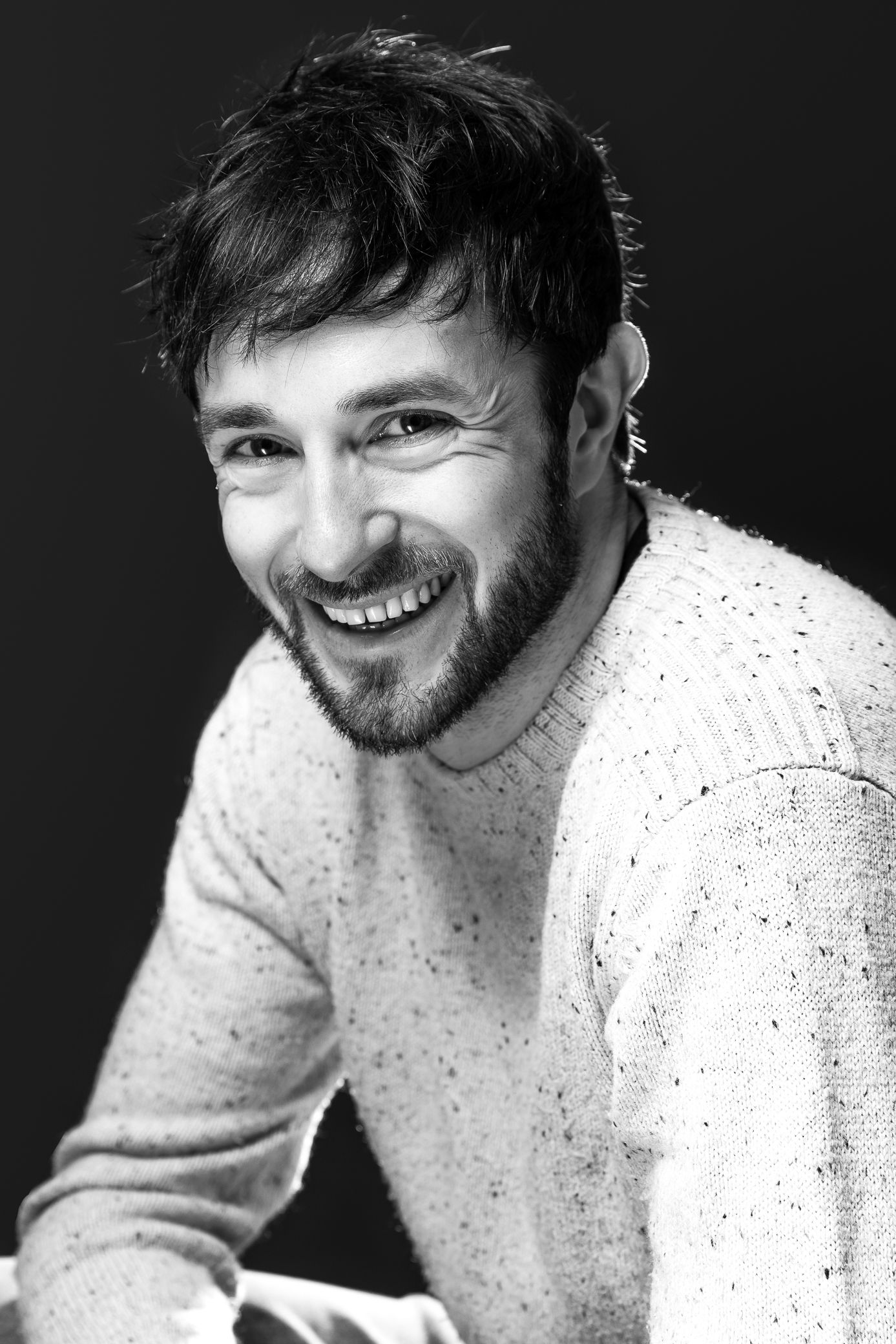 Black and white portrait of a smiling bearded man in a speckled sweater.
