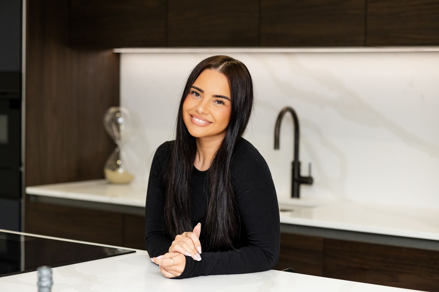 Young woman with long dark hair smiling at a white kitchen island with marble backsplash.