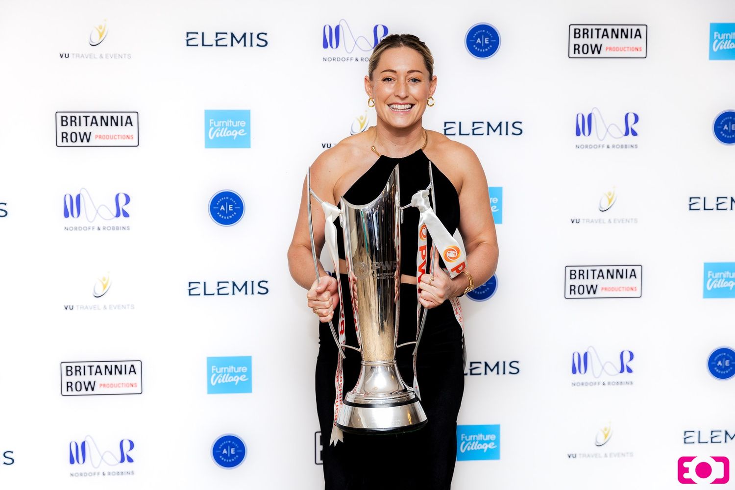 Woman in black dress holding trophy and award at Britannia Row and Elemis sponsored event.