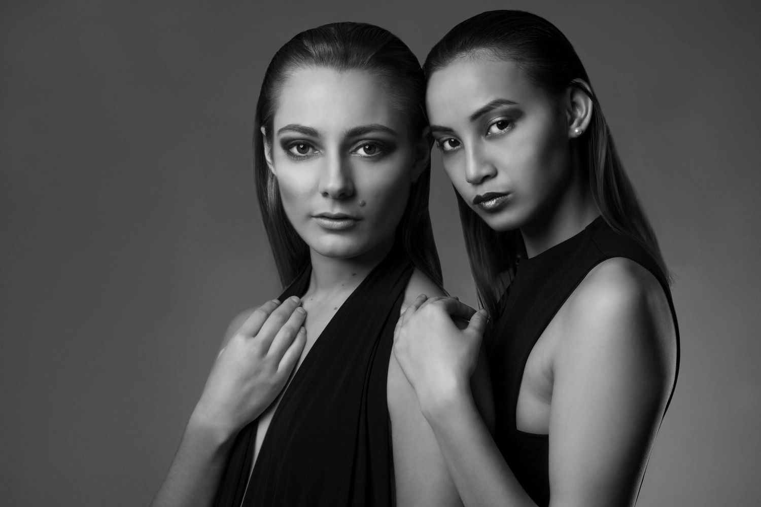 Black and white portrait of two young women in dark outfits posing together against a gray background.