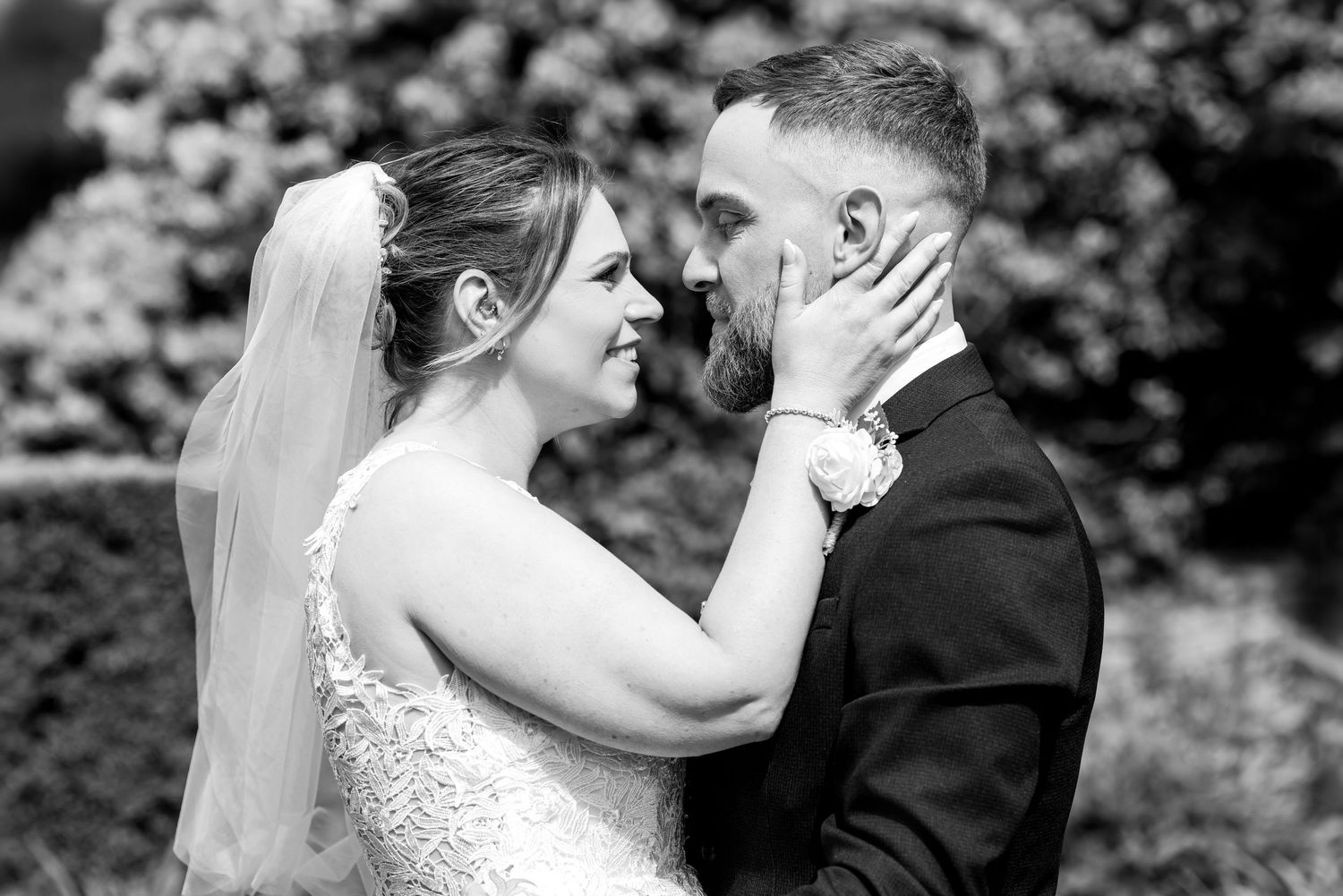 Black and white wedding photo of bride and groom sharing a tender moment, bride in lace gown and veil touching grooms face.