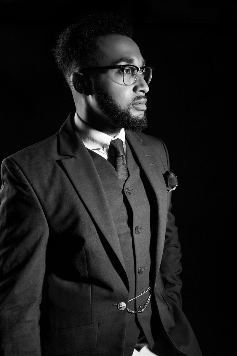 Sophisticated black and white portrait of a bearded man in a three-piece suit and glasses.