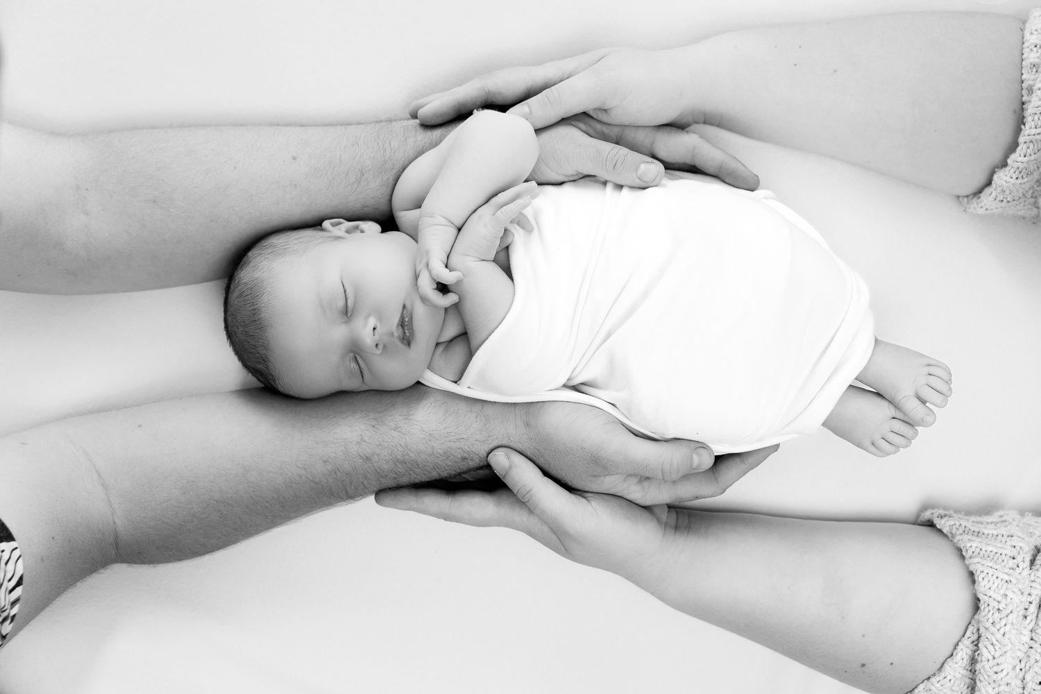Newborn baby sleeping peacefully while being gently held by both parents hands in black and white.