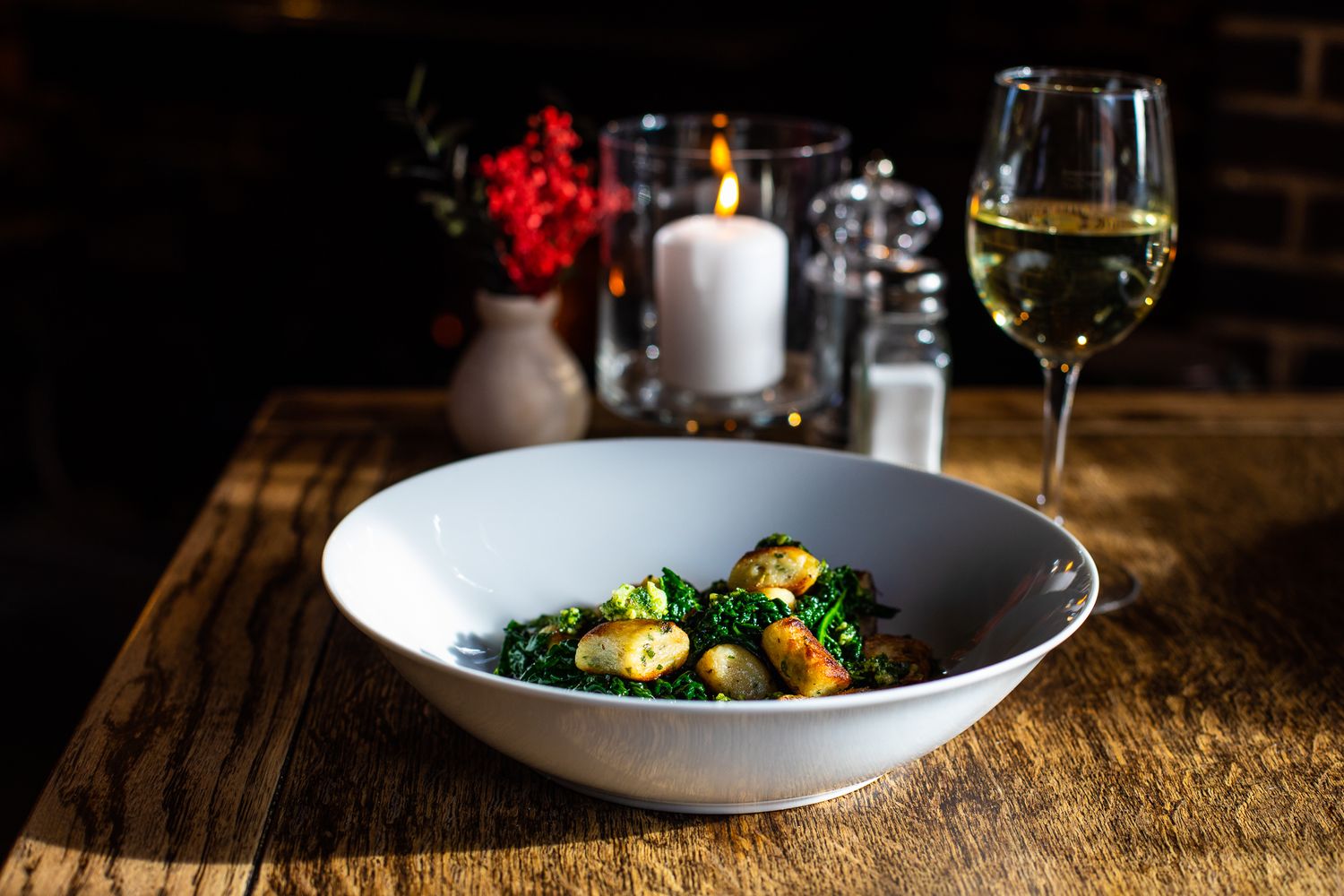 Gourmet bowl of sauteed Brussels sprouts and greens served with white wine in candlelit restaurant.