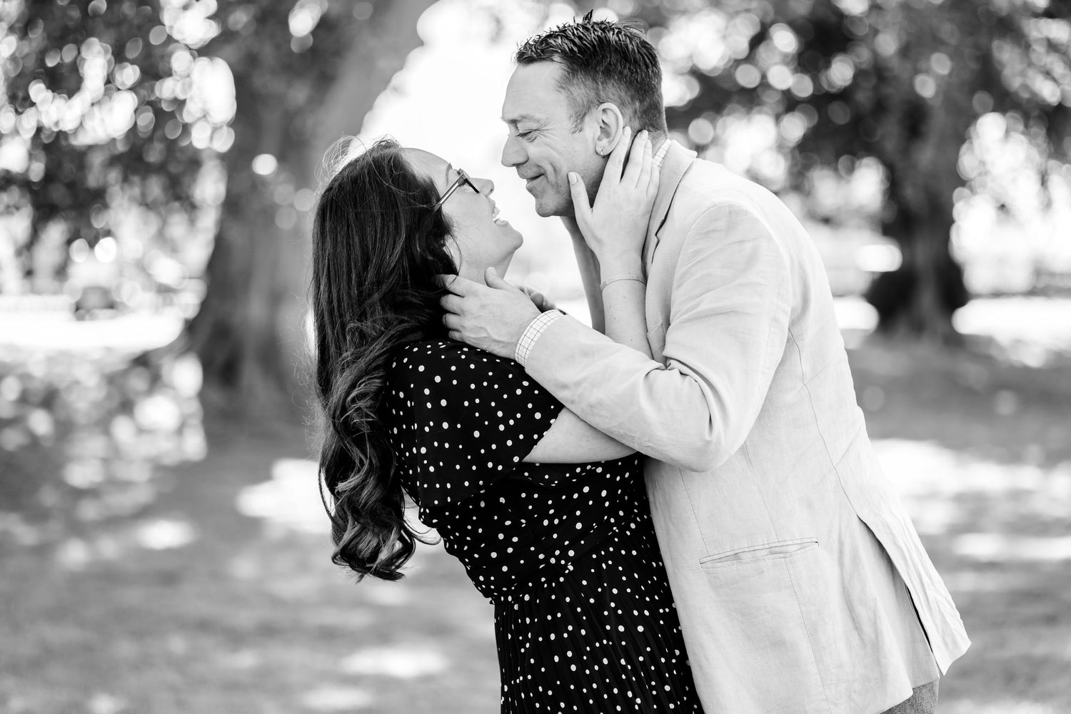 Black and white photo of a couple laughing and embracing outdoors under a large tree.