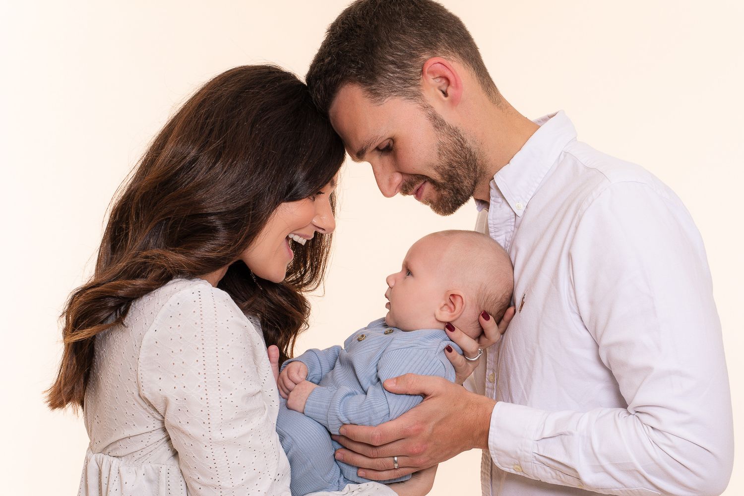 Loving couple with dark hair smiling at their newborn baby dressed in blue.