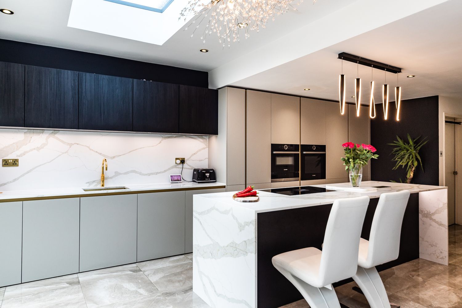 Stylish modern kitchen featuring marble backsplash, dark cabinetry, gold tap, and pendant lighting.