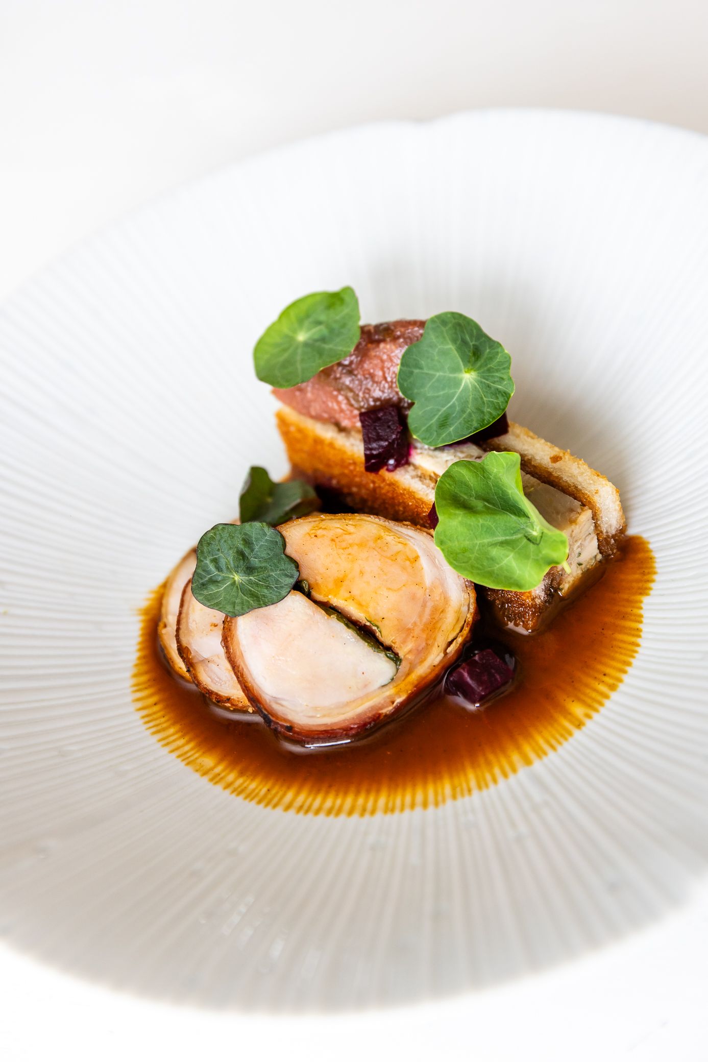 Elegant fine dining meat dish with nasturtium leaves and rich jus on white plate.