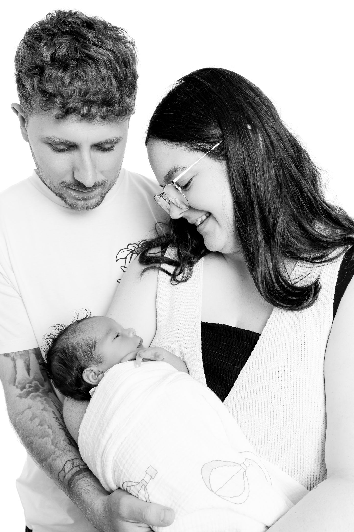 New parents smiling and holding their swaddled newborn baby, black and white studio photo.