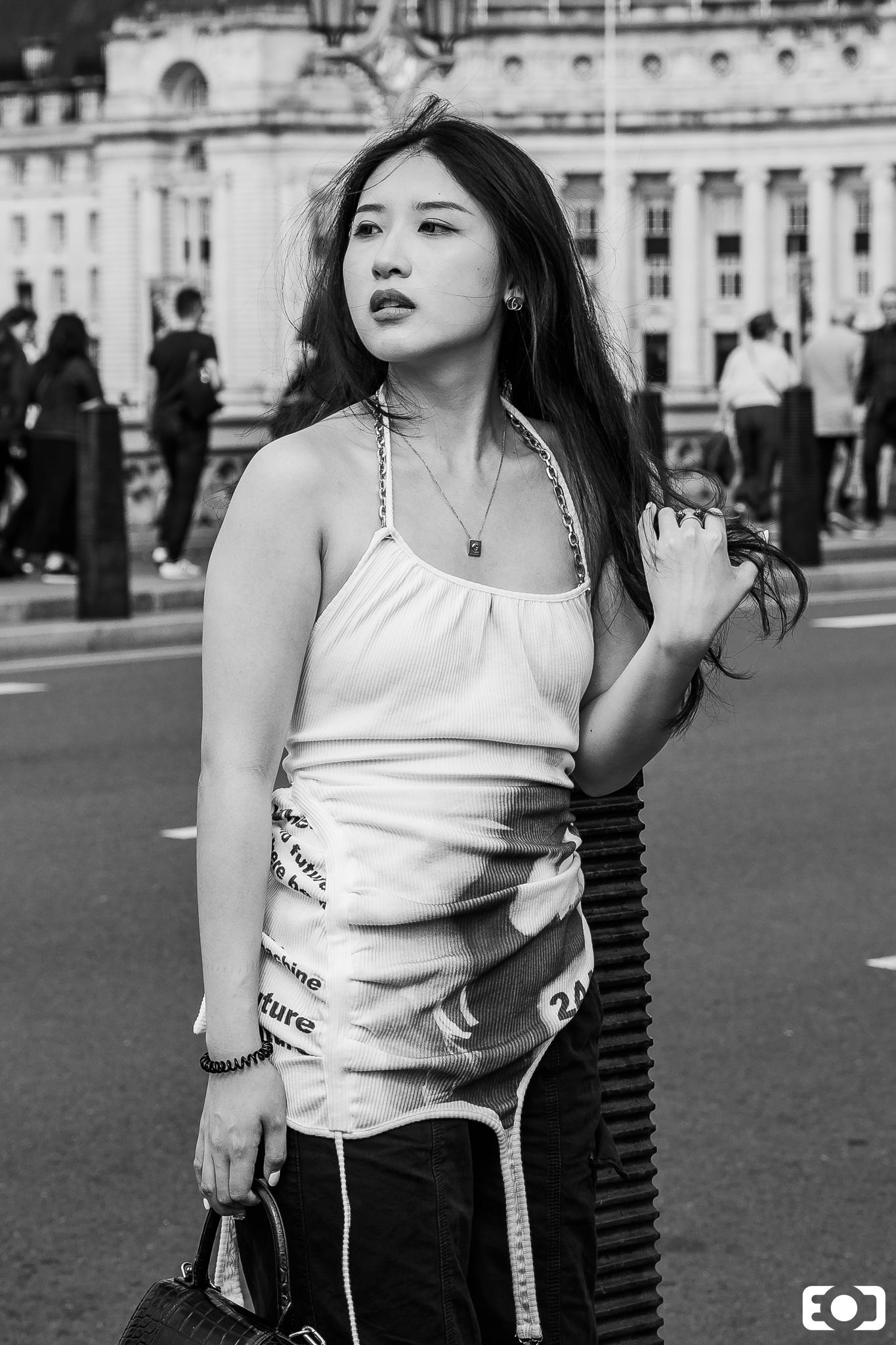 Young Asian woman in white top posing on a busy street with a grand building backdrop.